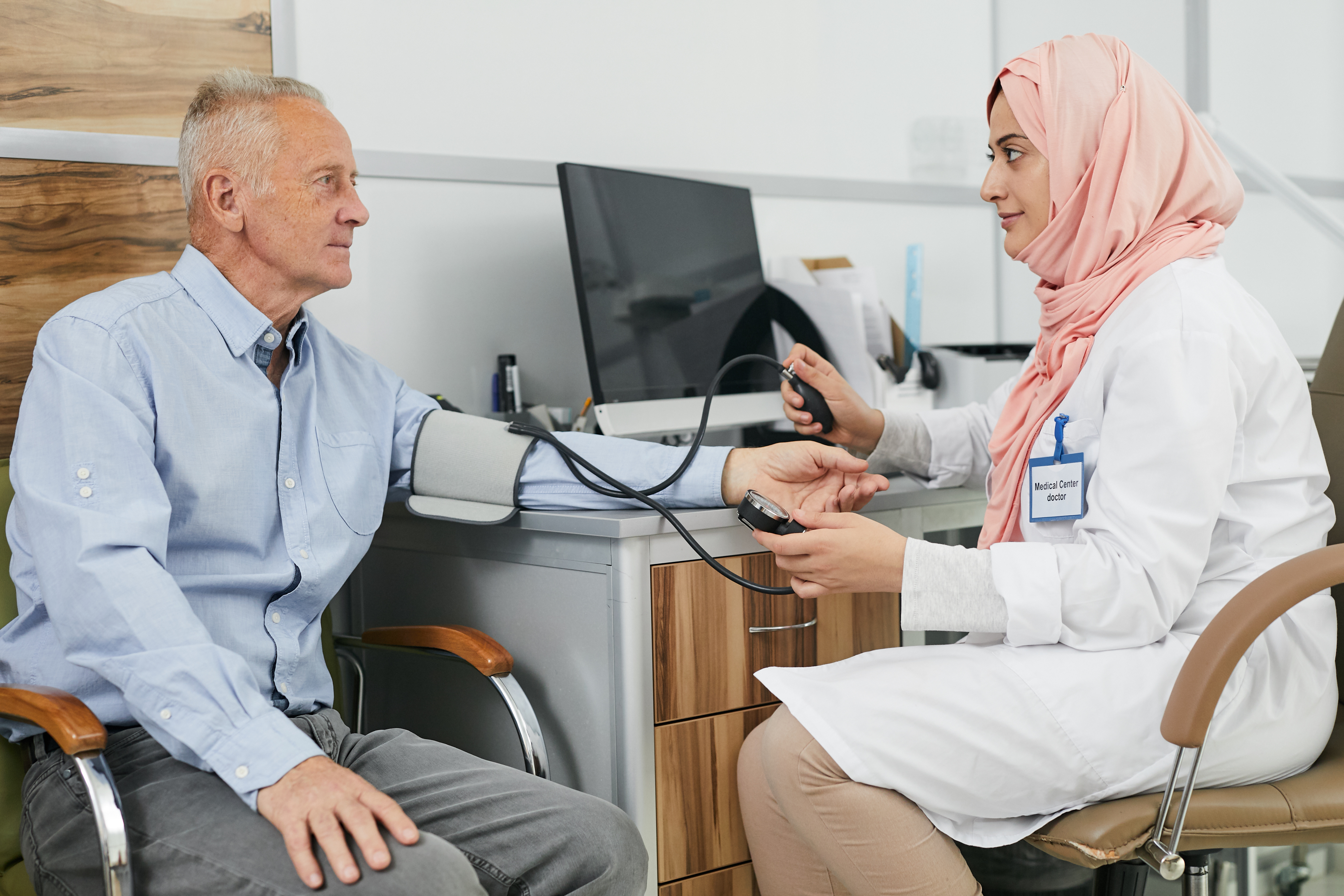 Middle Eastern Female Doctor Talking To Senior Patient Merit 